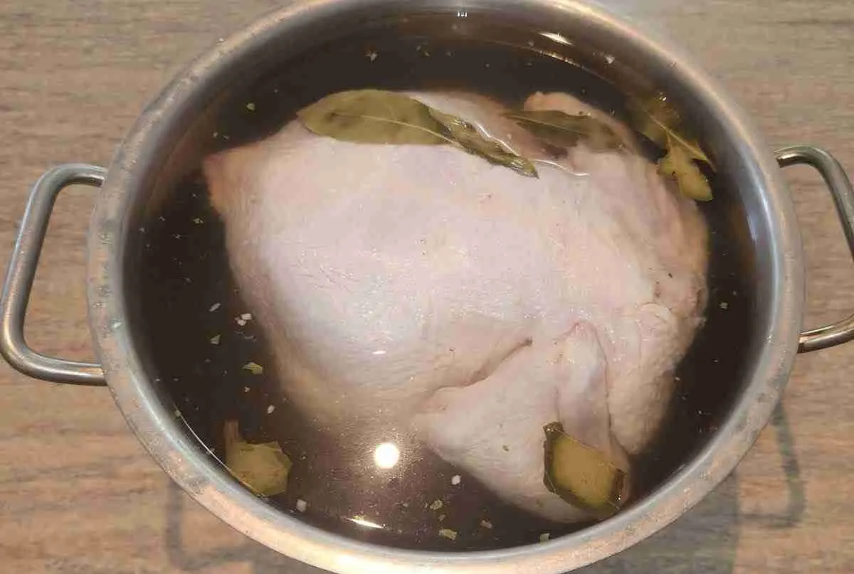 Brined-chicken Raw chicken submerged in a brine solution with bay leaves in a stainless steel pot.