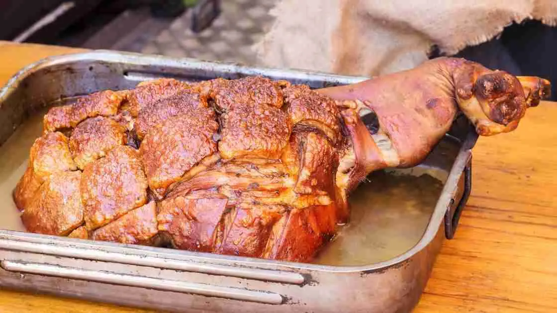 A whole smoked ham with crispy skin in a smoking pan.