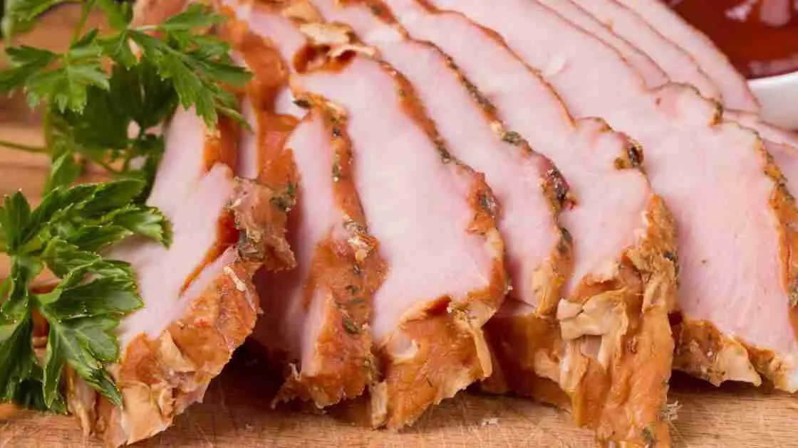 Sliced glazed ham on a festive table with side dishes.