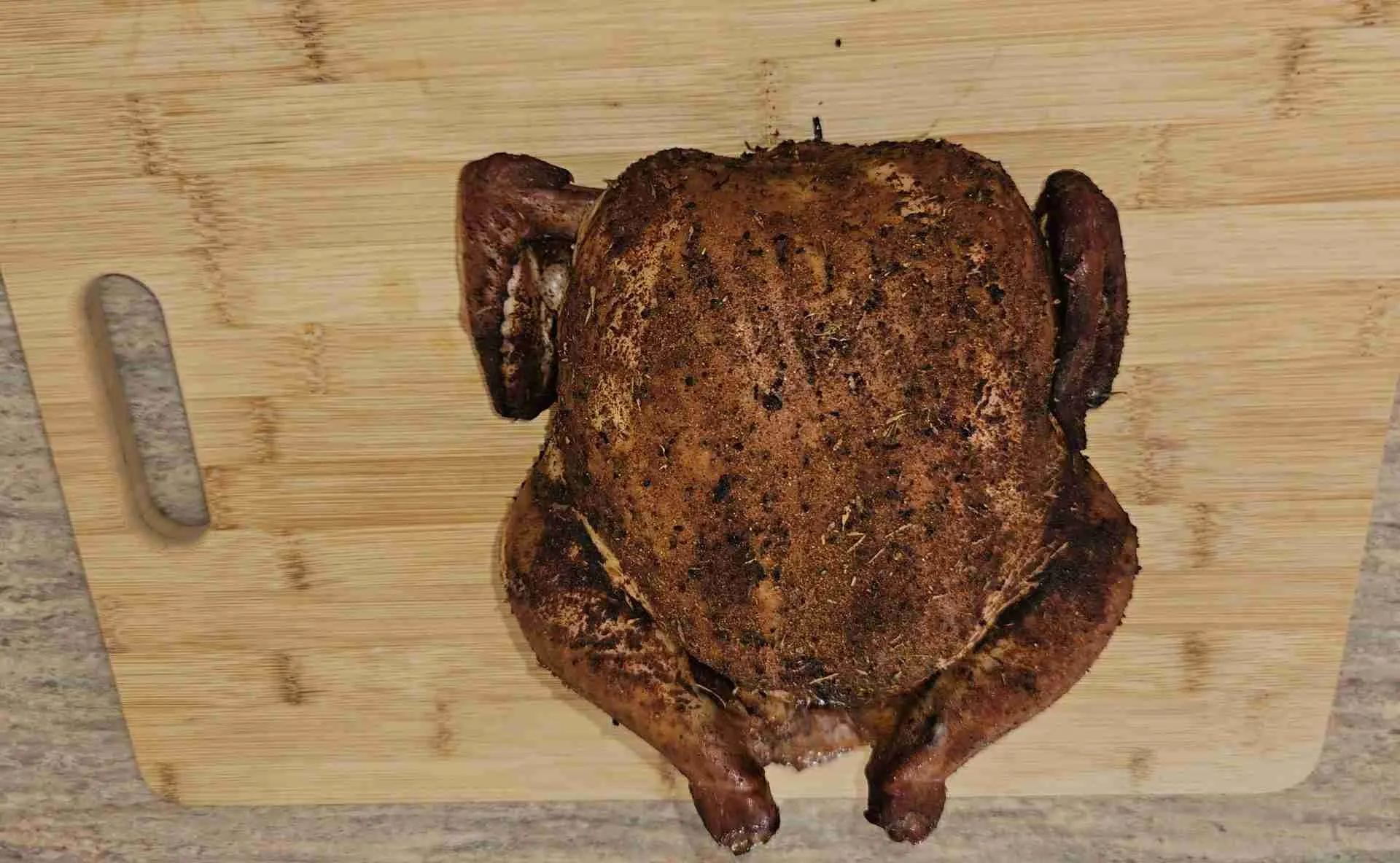 Smoked-chicken Well-seasoned smoked chicken with a crispy skin on a bamboo cutting board.