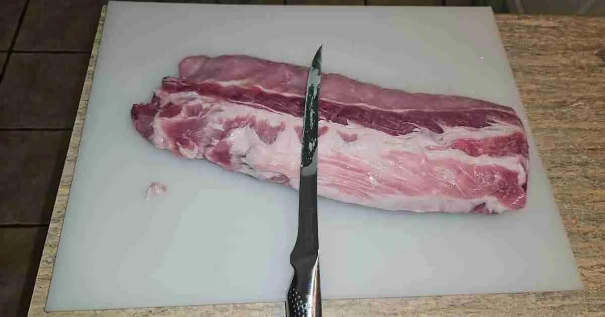 Pork-ribs A pre-trimmed rack of pork ribs on a gray cutting board with a boning knife, illustrating the initial step of fat trimming before smoking.