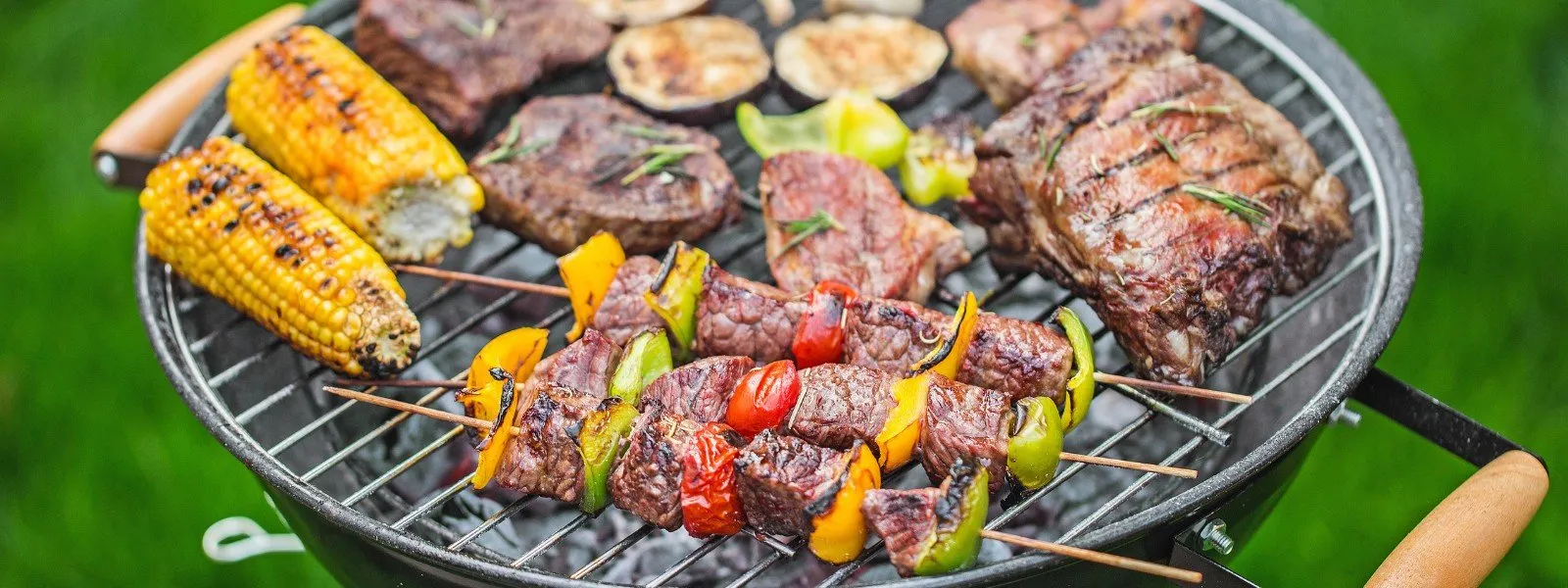 Feast-on-grill Assorted grilled meats including steaks and kebabs with vegetables, and corn on the cob on a charcoal grill, evoking a backyard BBQ atmosphere.