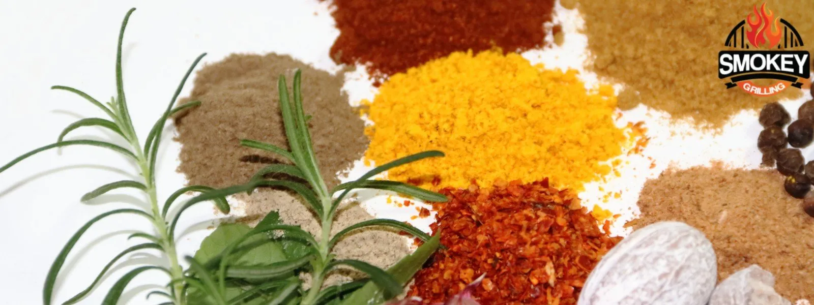Various spices and herbs arranged on a white background, including rosemary, bay leaves, black pepper, turmeric, paprika, and more, with the Smokey Grilling logo in the top right corner.