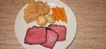 Smoked corned beef slices on a plate with cabbage, baby potatoes, and carrots, showcasing a deliciously smoked dinner.